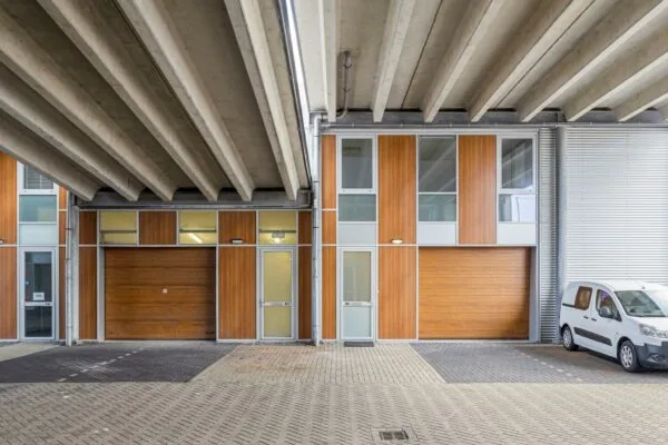 Bedrijfspanden aan de Tijnmuiden met houten gevelbekleding en een geparkeerd wit bestelbusje onder een betonnen viaduct.