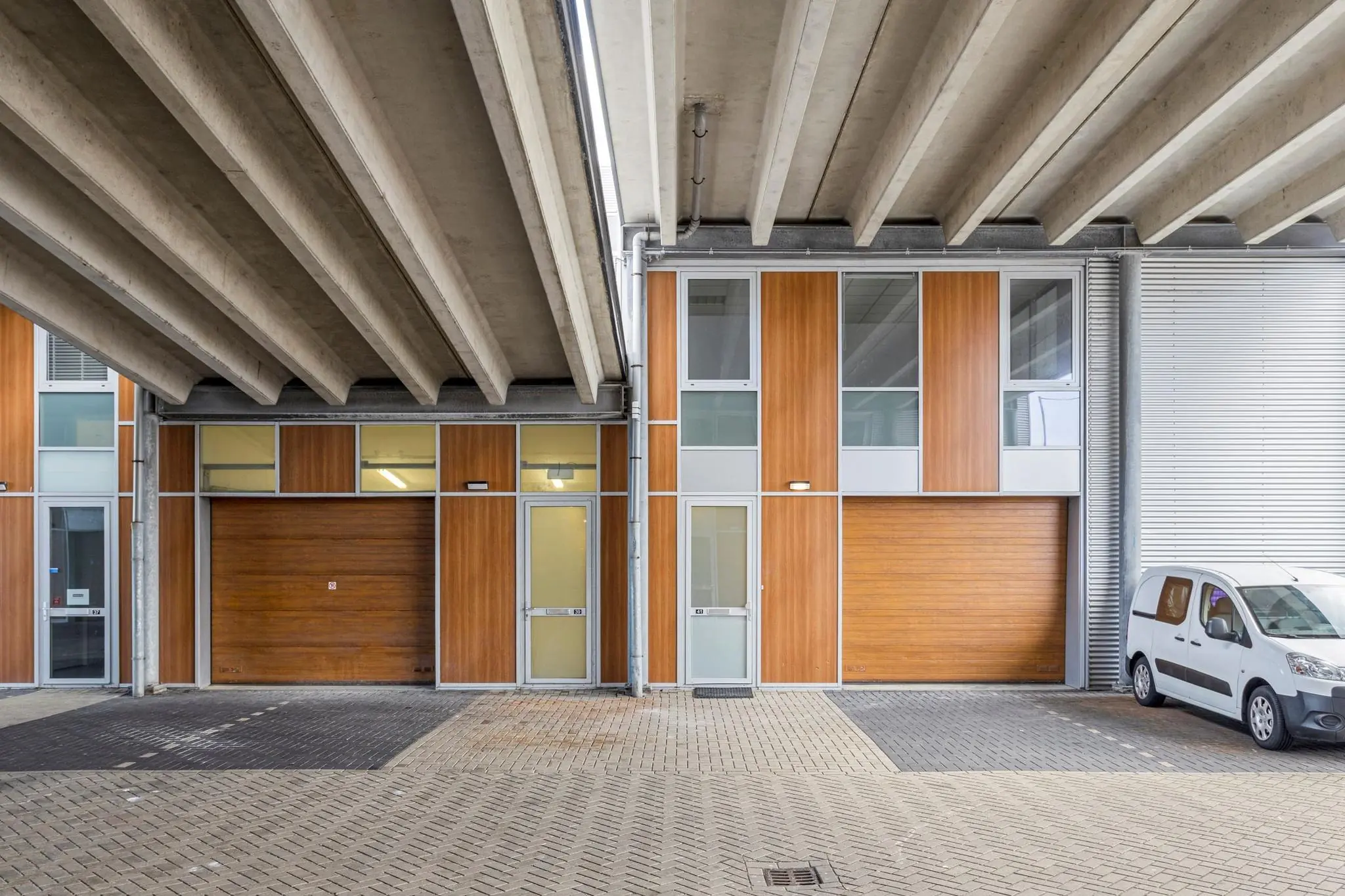 Bedrijfspanden aan de Tijnmuiden met houten gevelbekleding en een geparkeerd wit bestelbusje onder een betonnen viaduct.