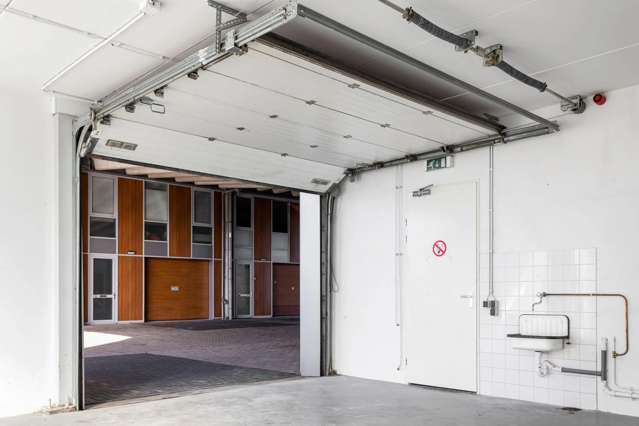 Openstaande garagedeur met zicht op een binnenplaats en houten gevels van bedrijfsunits aan de Tijnmuiden.