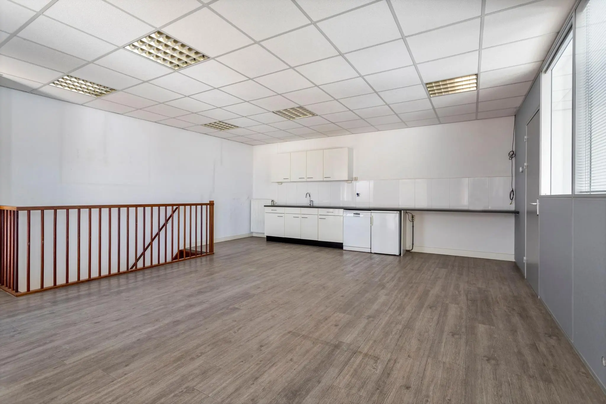 Ruime, lichte kantoorruimte aan de Tijnmuiden met een kitchenette, houten trapleuning en grijze laminaatvloer.