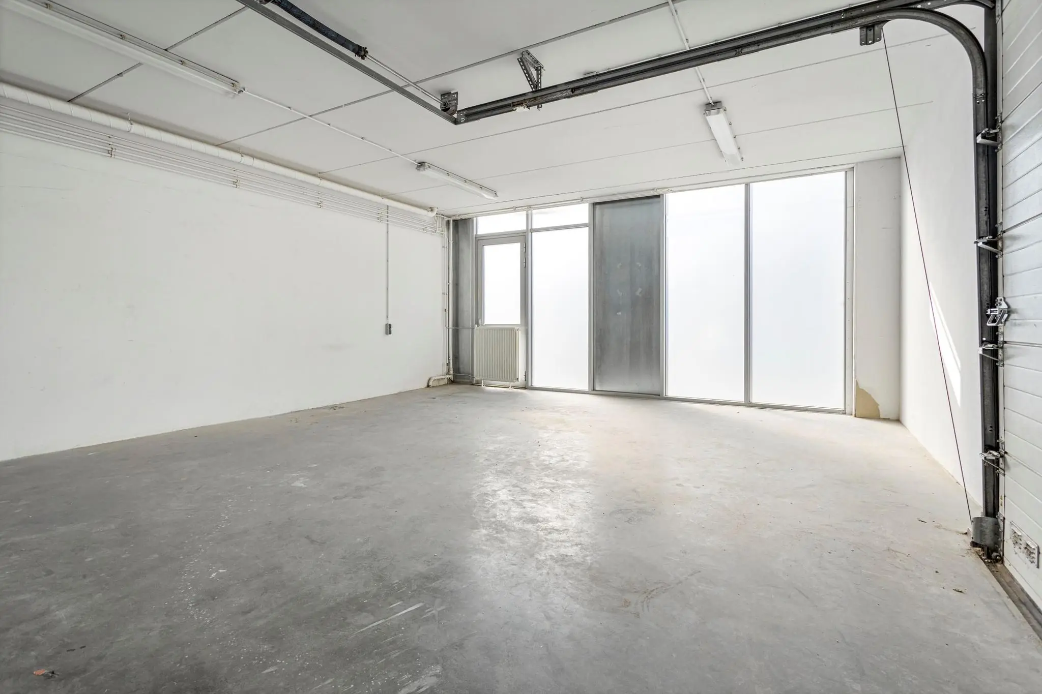 Leeg industrieel magazijn met betonnen vloer en grote raampartij in Tijnmuiden.