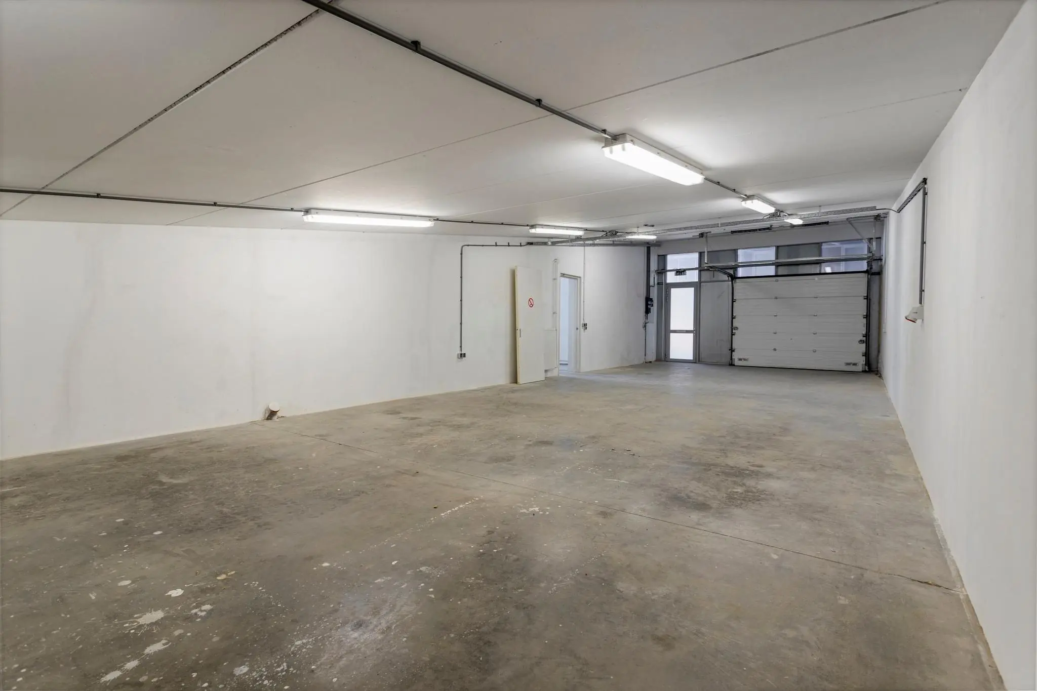 Lege, goed verlichte garage of bedrijfsruimte met betonnen vloer en witte muren aan de Tijnmuiden.