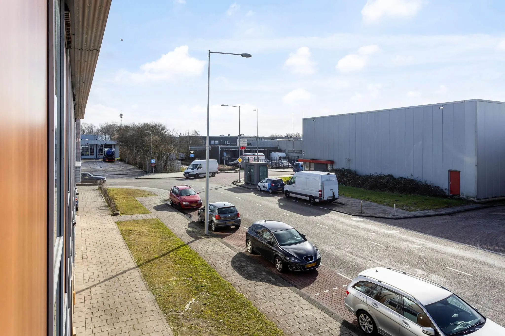 Straatbeeld van het industrieterrein Tijnmuiden in Amsterdam met geparkeerde auto's, een bushokje en bedrijfsgebouwen.