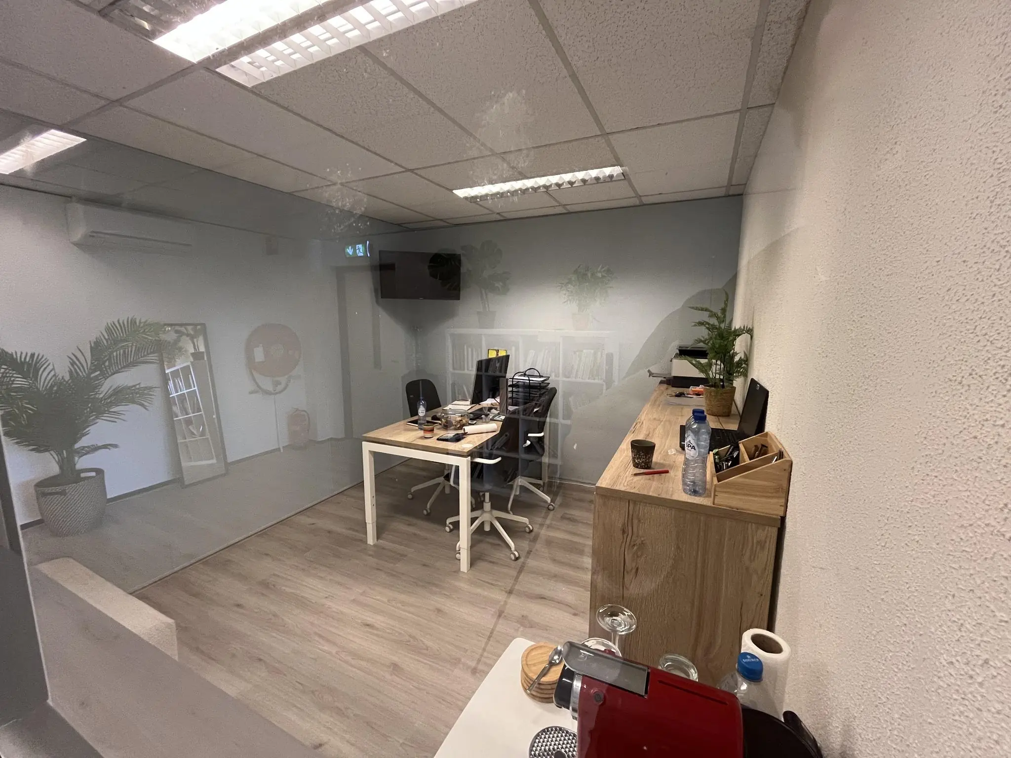 Modern kantoorinterieur aan de Hollantlaan met bureaus, planten en kantoorbenodigdheden, gezien door een glazen wand.
