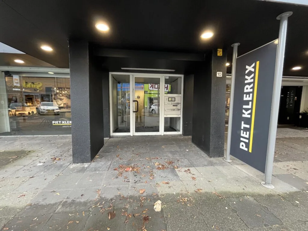 Ingang van het gebouw aan de Hollantlaan 10 met een bord van meubelwinkel Piet Klerkx.