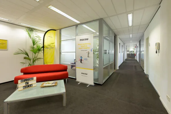 Ontvangstruimte van het Macaw-kantoor met een rode bank, een banner en een glazen vergaderruimte.