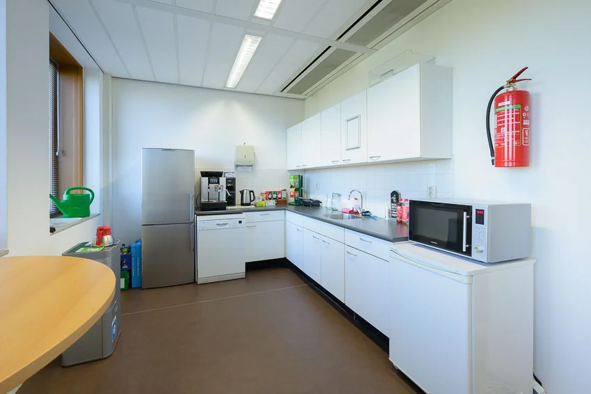 Moderne kantoorkeuken in Trondheim met witte kasten, magnetron, koffiezetapparaat en brandblusser aan de muur.