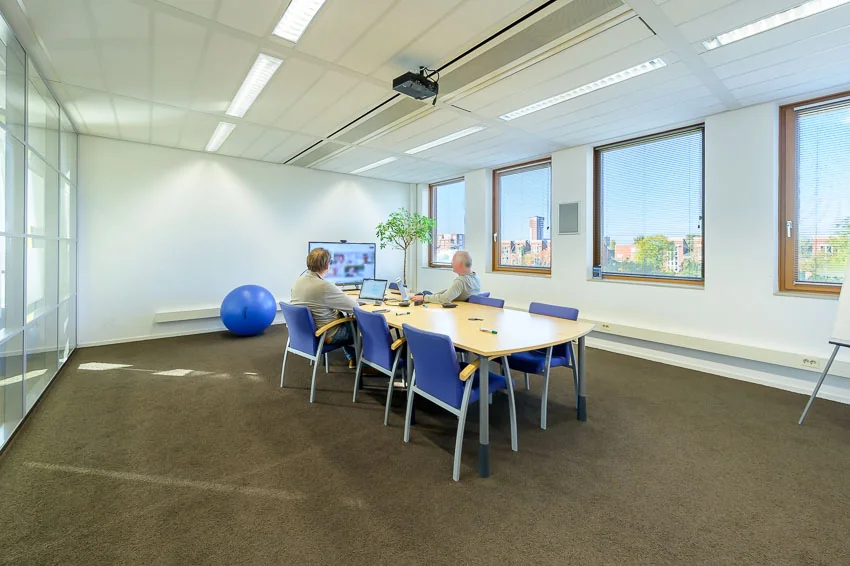 Twee mannen zitten in een moderne vergaderruimte in Trondheim en videobellen met collega’s via een groot scherm.