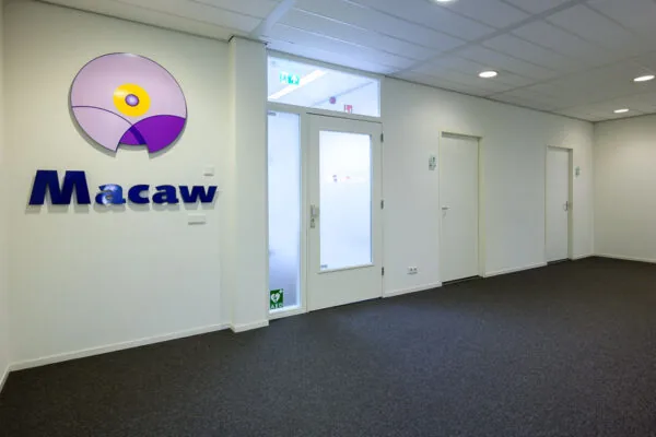 Ingang van een modern kantoorpand met het logo en de naam van Macaw op de muur.