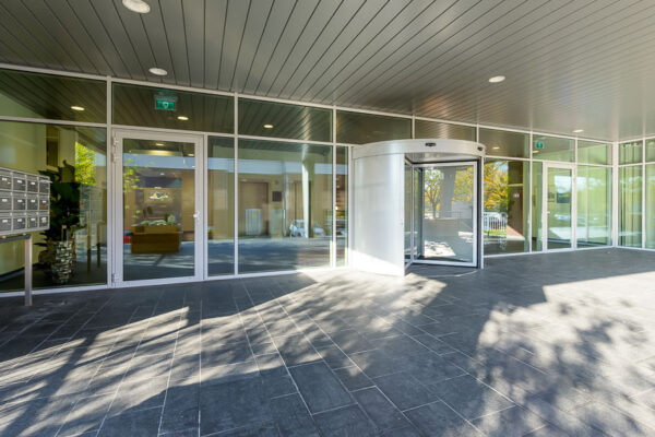 Entree van een modern gebouw in Trondheim met glazen gevel, grijze vloertegels en een draaideur.