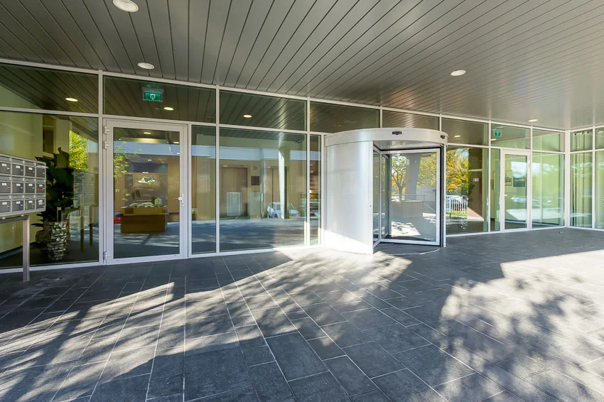 Entree van een modern gebouw in Trondheim met glazen gevel, grijze vloertegels en een draaideur.