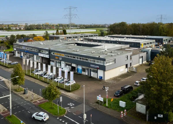 Bedrijventerrein aan de Hoofdweg met meerdere bedrijfsunits, geparkeerde auto's en vlaggen langs de straat.