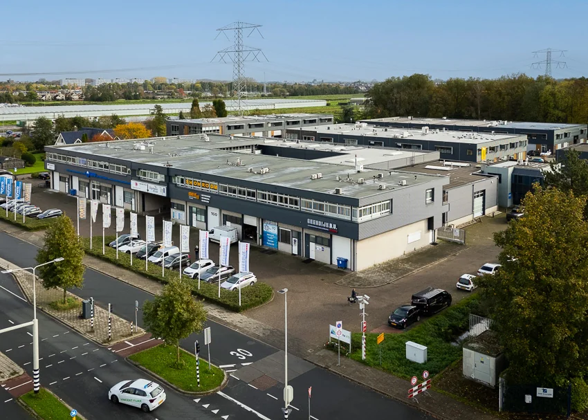 Bedrijventerrein aan de Hoofdweg met meerdere bedrijfsunits, geparkeerde auto's en vlaggen langs de straat.