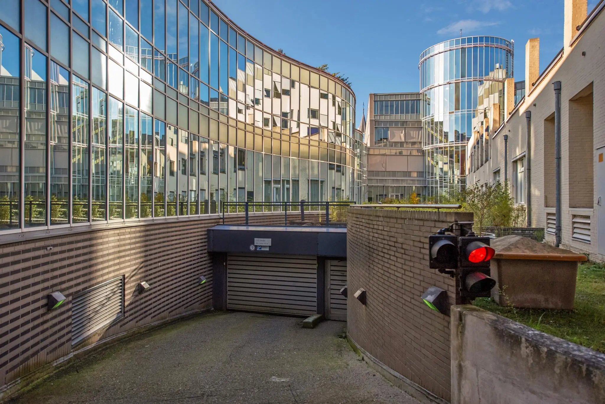 Gebogen glazen kantoorgevels weerspiegelen de omgeving boven een gesloten parkeergarage aan de Doelenstraat.