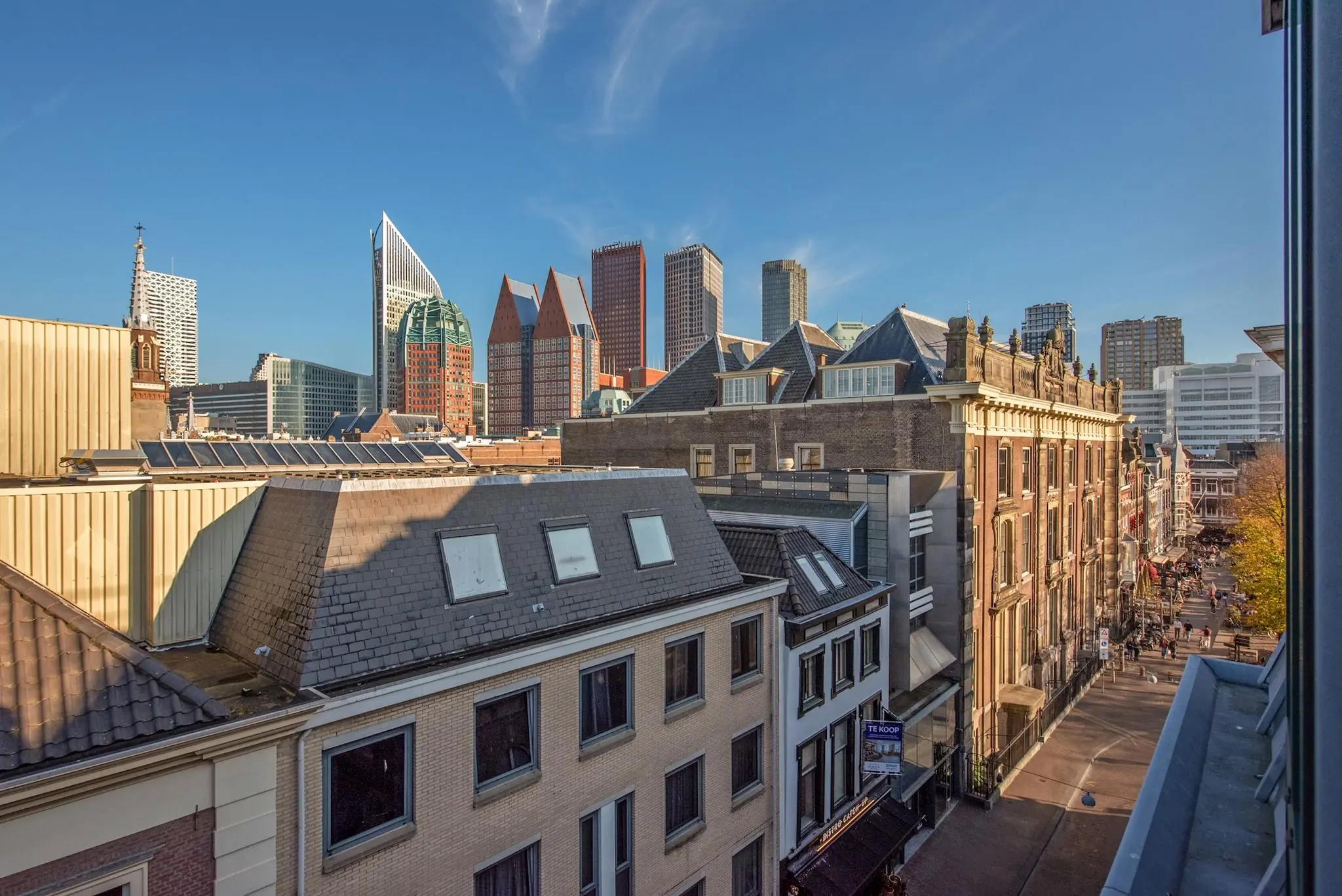 Zonnig uitzicht op de Doelenstraat in Den Haag met historische panden op de voorgrond en moderne hoogbouw op de achtergrond.