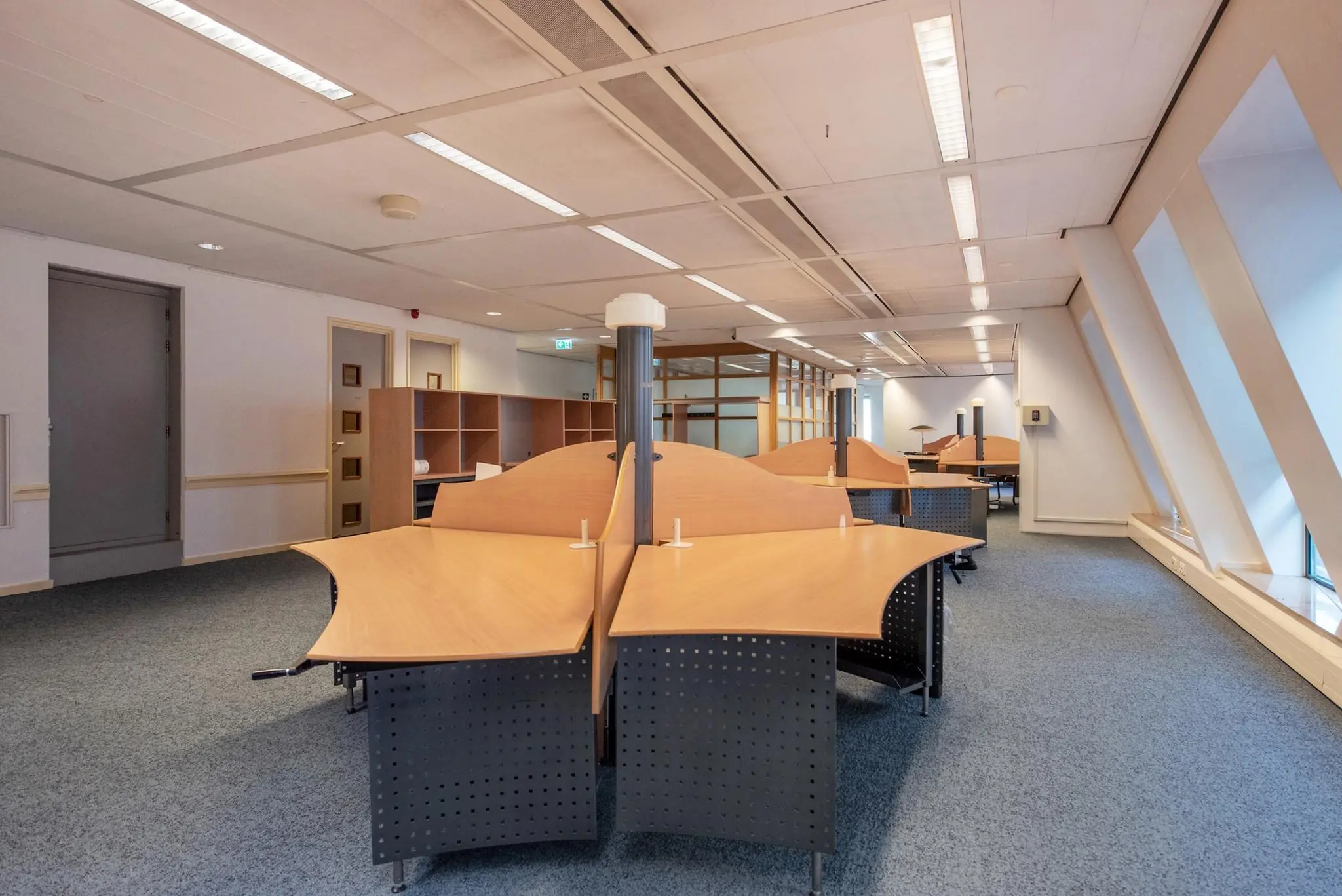 Kantoorruimte met meerdere lege werkplekken en grote ramen aan de rechterzijde in de Doelenstraat.