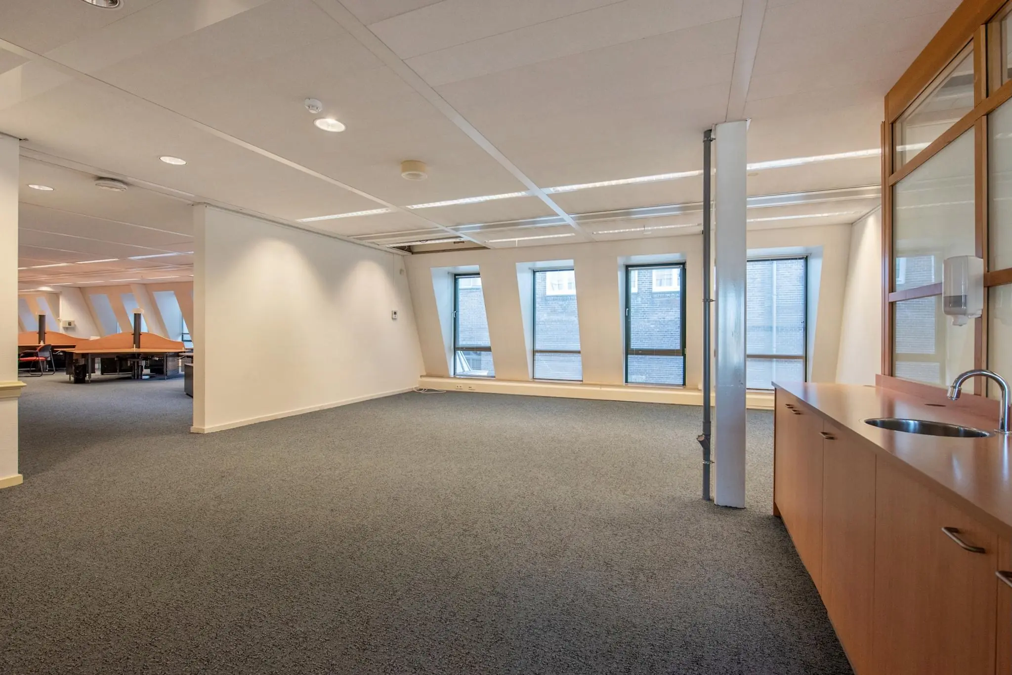 Ruim en licht kantoorinterieur aan de Doelenstraat met tapijtvloer, schuine ramen en een kitchenette.