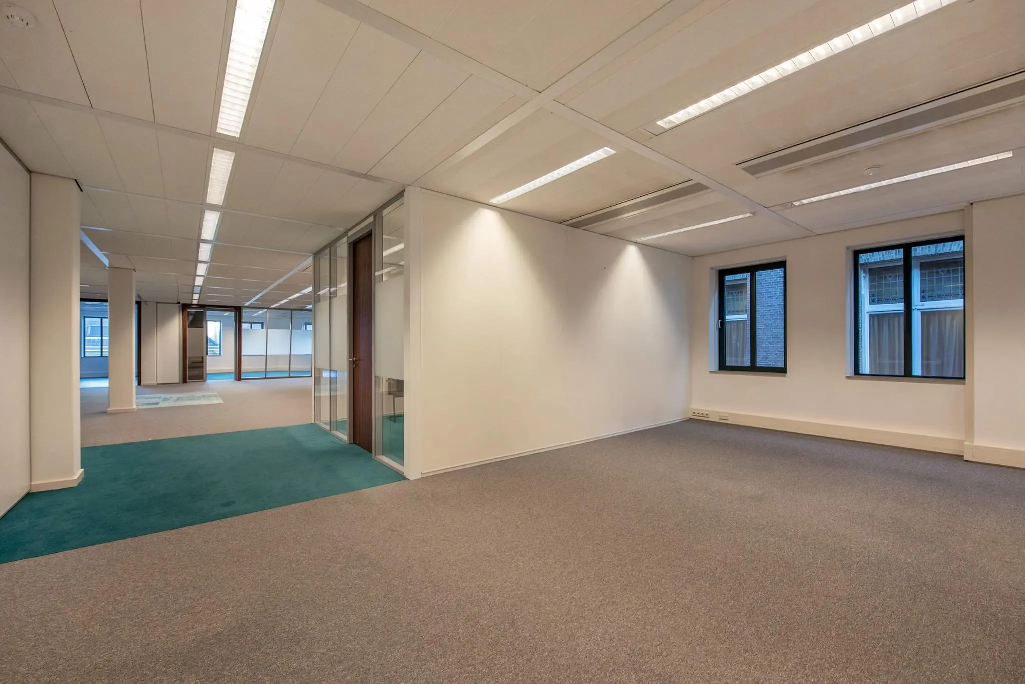 Leeg kantoorpand aan de Doelenstraat met systeemplafond, tapijtvloer en glazen kantoorruimte.