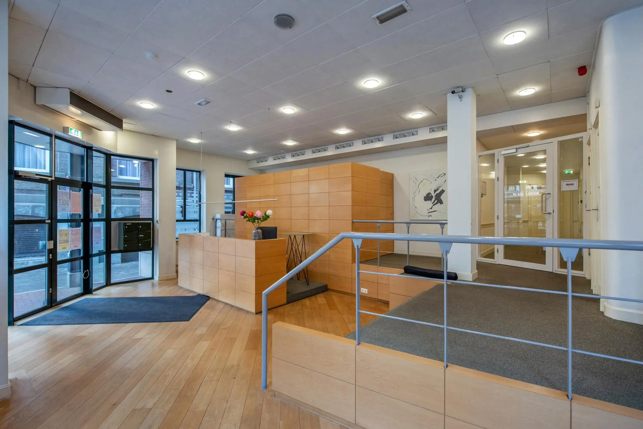 Moderne entreehal van een kantoorgebouw aan de Doelenstraat met houten receptiebalie, glazen deuren en natuurlijke lichtinval.