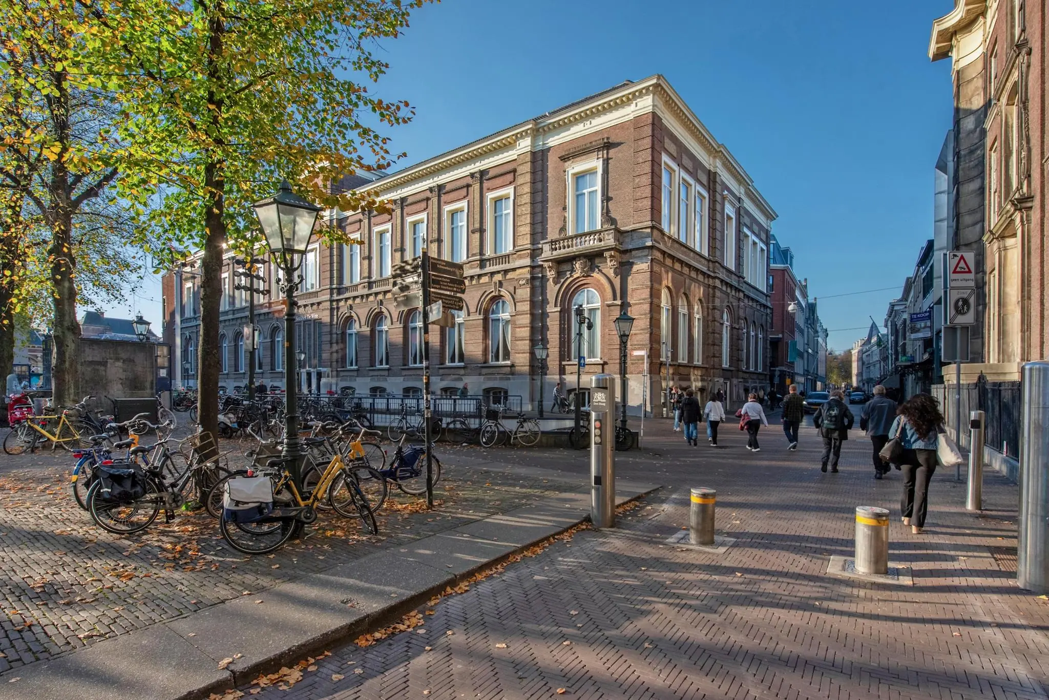 Straatbeeld van de Doelenstraat in een historisch stadscentrum met klassieke gebouwen, fietsen en voetgangers op een zonnige dag.