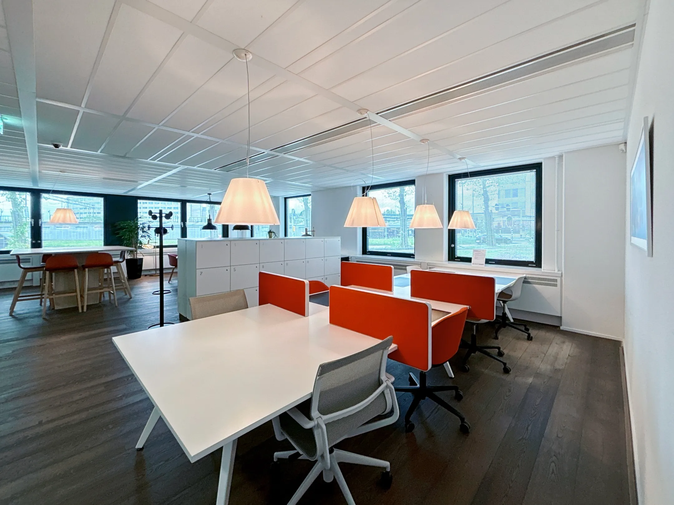 Een moderne en lichte kantoorruimte met witte bureaus, oranje stoelen en hanglampen.