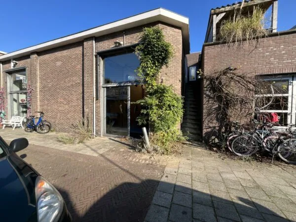Vooraanzicht van een laag gebouw aan de Kerkstraat met grote ramen, fietsen en een trap naar boven.