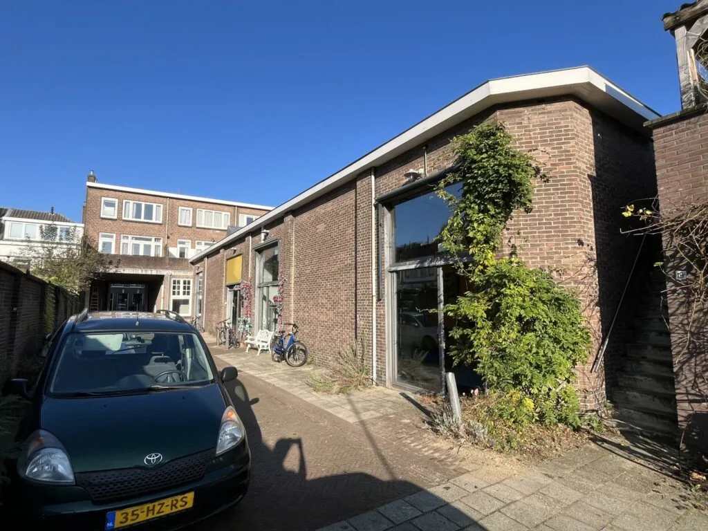 Bakstenen pand aan de Kerkstraat met grote ramen, fietsen en een geparkeerde auto op de voorgrond.