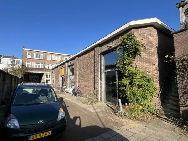Bakstenen pand aan de Kerkstraat met grote ramen, fietsen en een geparkeerde auto op de voorgrond.