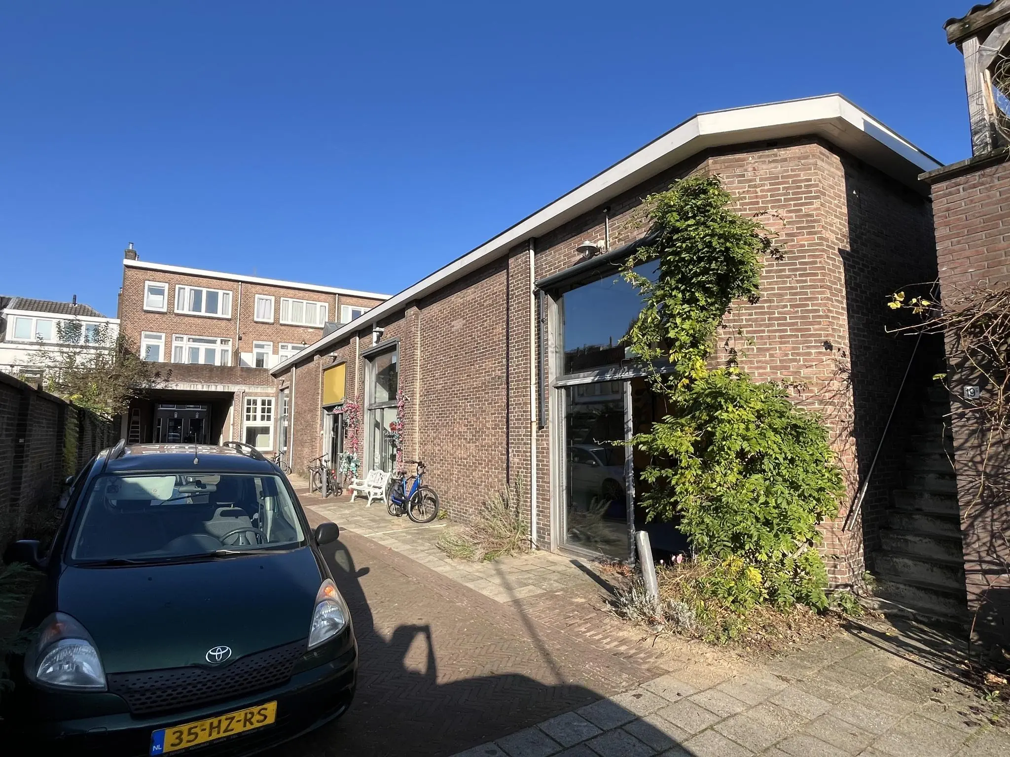 Bakstenen pand aan de Kerkstraat met grote ramen, fietsen en een geparkeerde auto op de voorgrond.