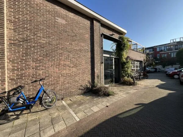 Ingang van een bakstenen gebouw aan de Kerkstraat met fietsen en geparkeerde auto's op de achtergrond.