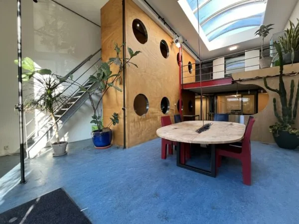 Moderne, lichtovergoten ruimte aan de Kerkstraat met ronde eettafel, kleurrijke stoelen, grote planten en een vide met dakraam.