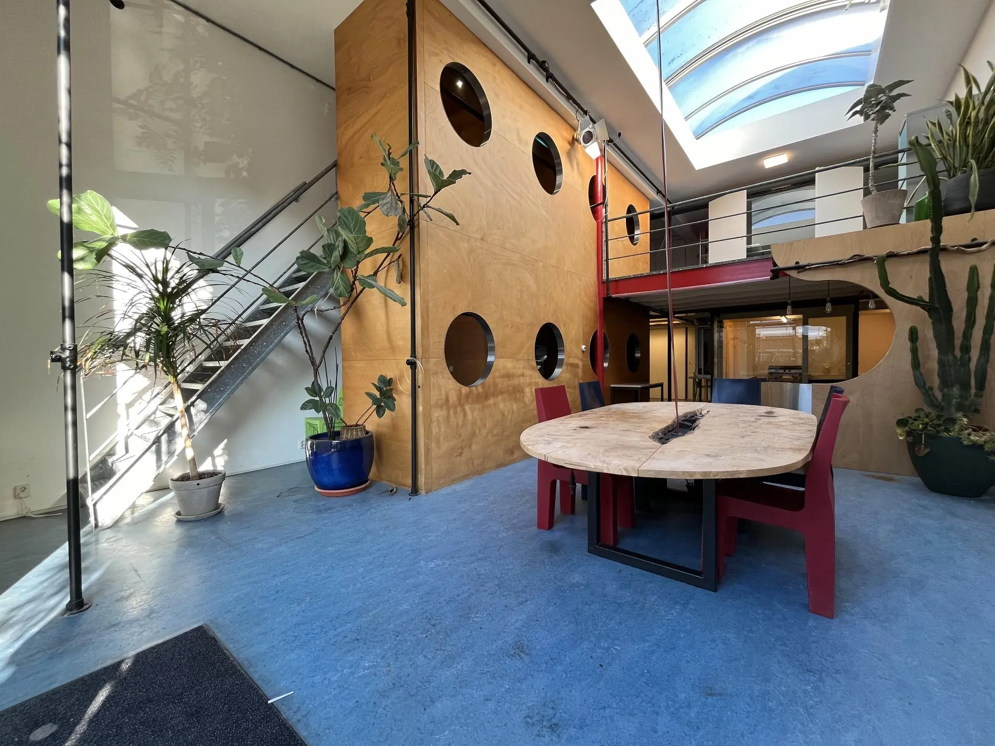 Moderne, lichtovergoten ruimte aan de Kerkstraat met ronde eettafel, kleurrijke stoelen, grote planten en een vide met dakraam.