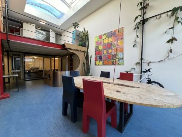 Moderne gemeenschappelijke ruimte aan de Kerkstraat met een ovale houten tafel, kleurrijke stoelen, kunst aan de muur en veel daglicht via een glazen dak.