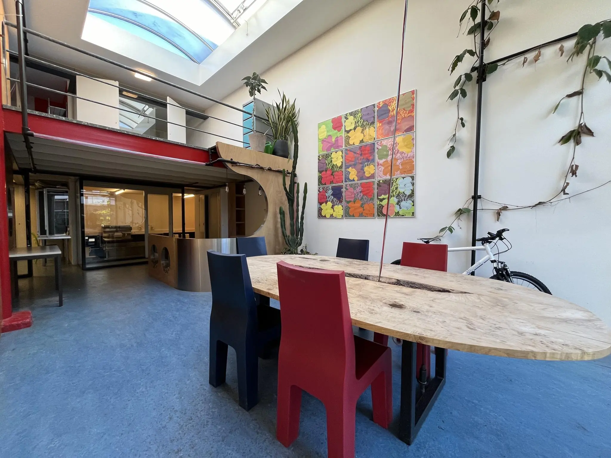 Moderne gemeenschappelijke ruimte aan de Kerkstraat met een ovale houten tafel, kleurrijke stoelen, kunst aan de muur en veel daglicht via een glazen dak.
