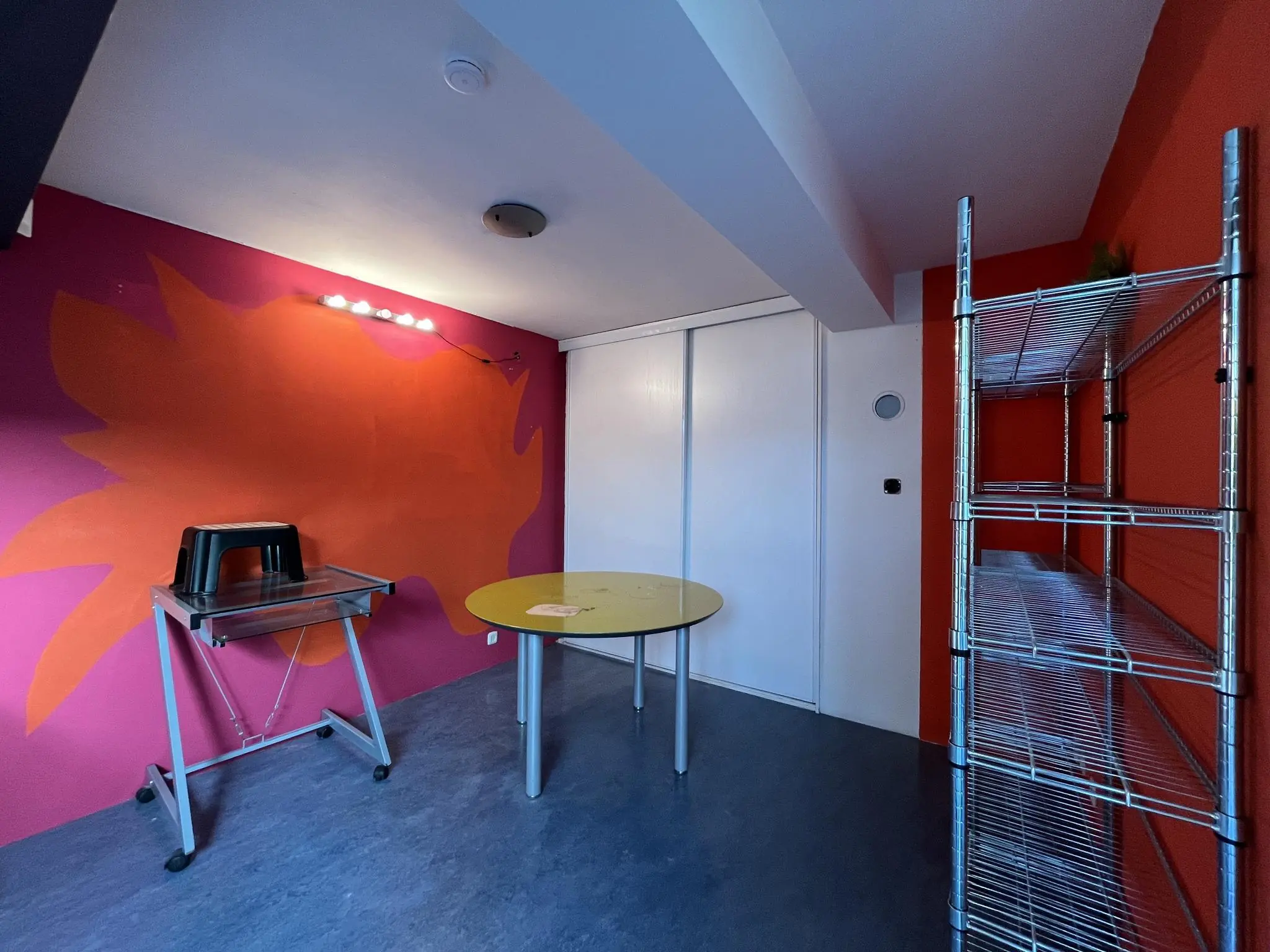 Kleine kleurrijke kamer aan de Kerkstraat met een metalen rek, geel tafeltje en opvallende muurschildering.