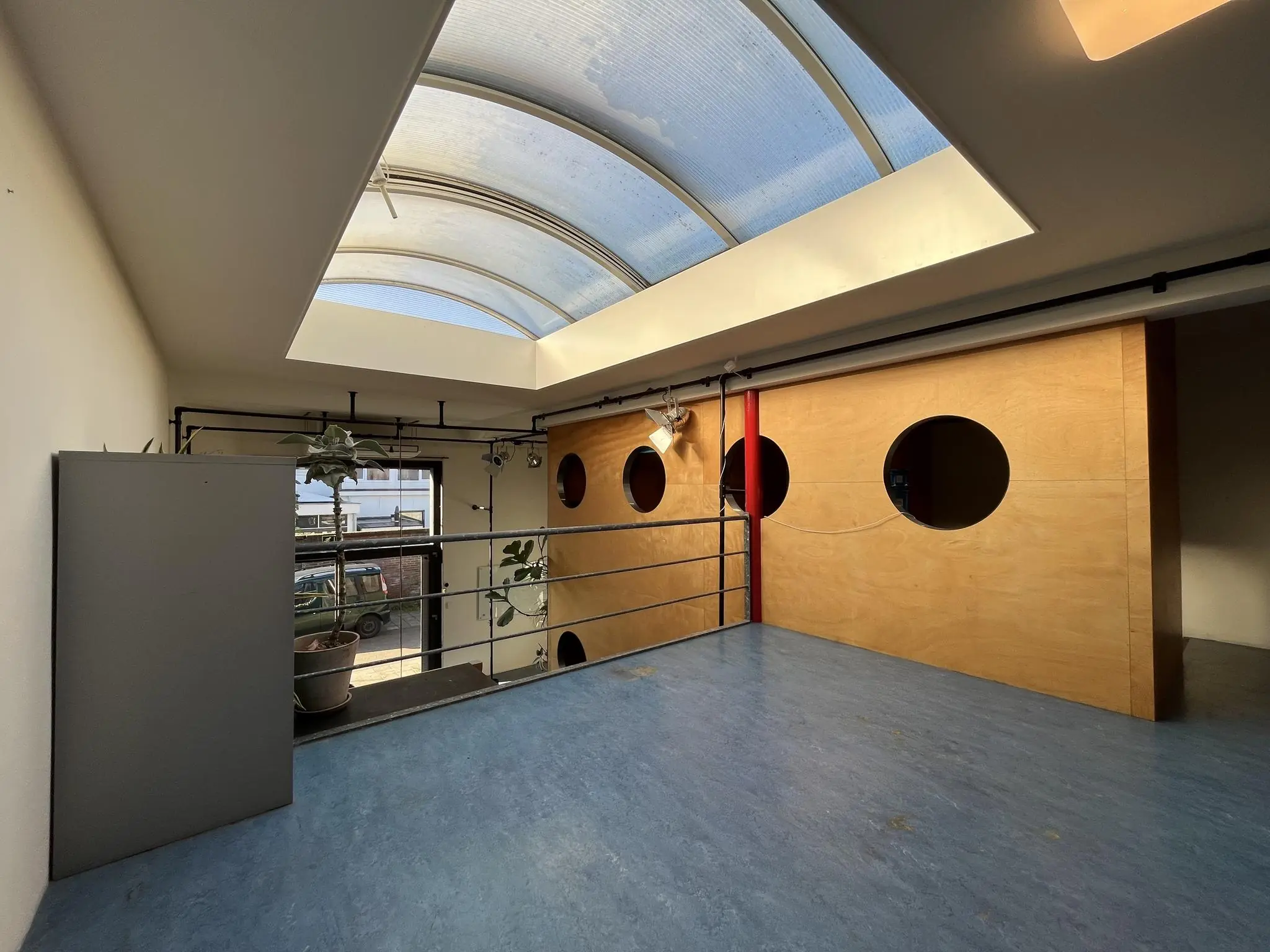 Binnenruimte in een modern gebouw aan de Kerkstraat met lichtblauwe vloer, houten wand met ronde ramen en een groot gebogen dakraam.