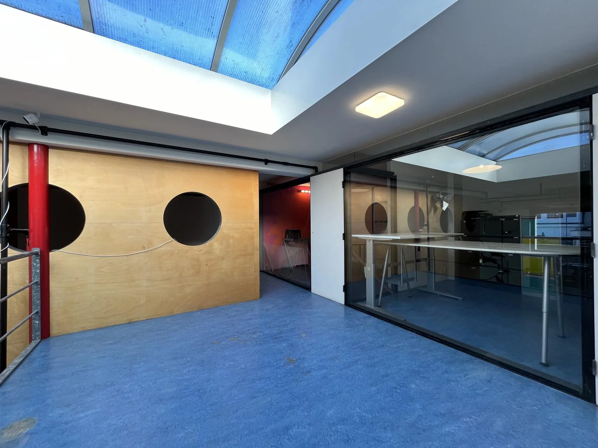 Interieur van een modern kantoor aan de Kerkstraat met blauwe vloer, glazen wand en houten muur met ronde openingen.