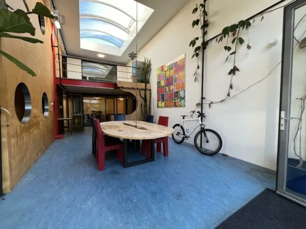 Moderne gemeenschappelijke ruimte aan de Kerkstraat met ronde tafel, rode stoelen, kunst aan de muur en een fiets tegen de wand.