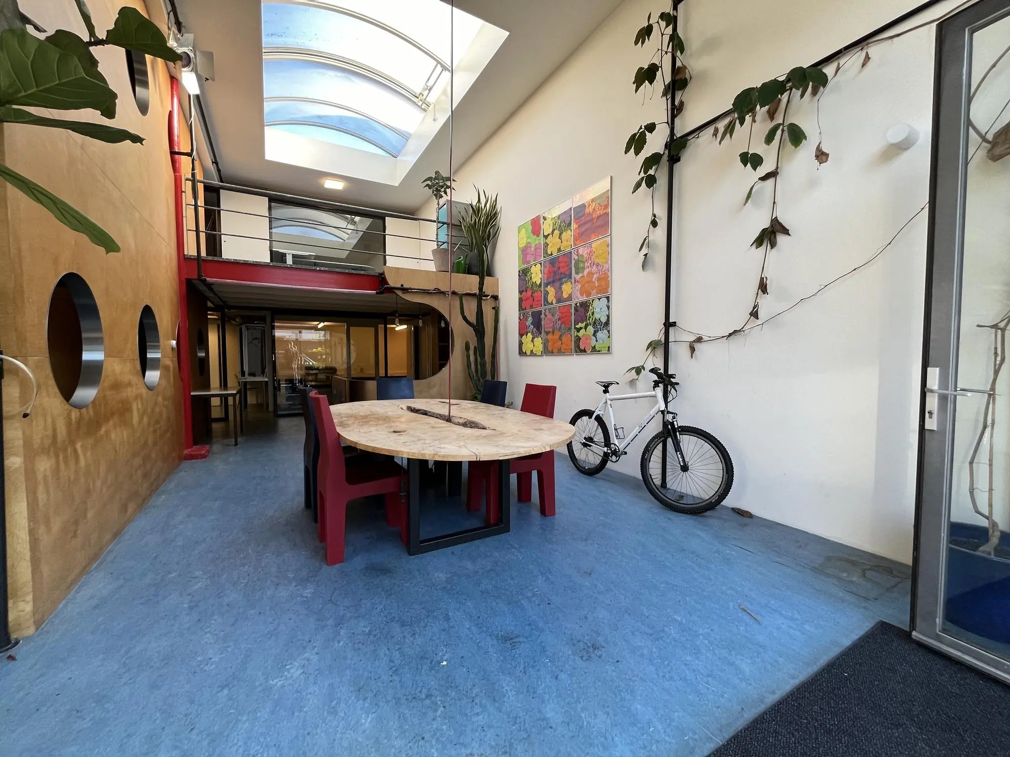 Moderne gemeenschappelijke ruimte aan de Kerkstraat met ronde tafel, rode stoelen, kunst aan de muur en een fiets tegen de wand.
