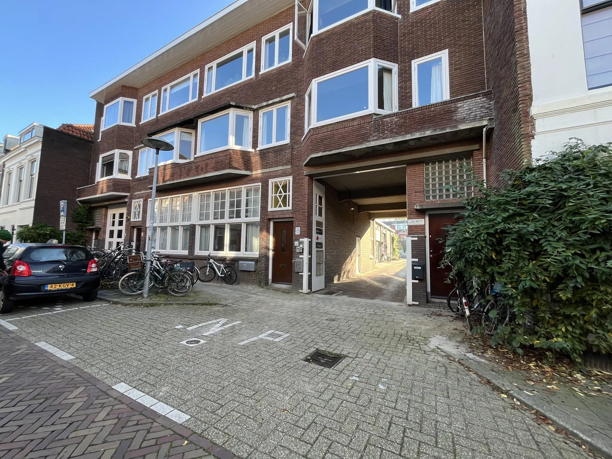 Straatbeeld van de Kerkstraat met een woongebouw, geparkeerde fietsen en auto’s, en een doorgang naar een binnenplaats.