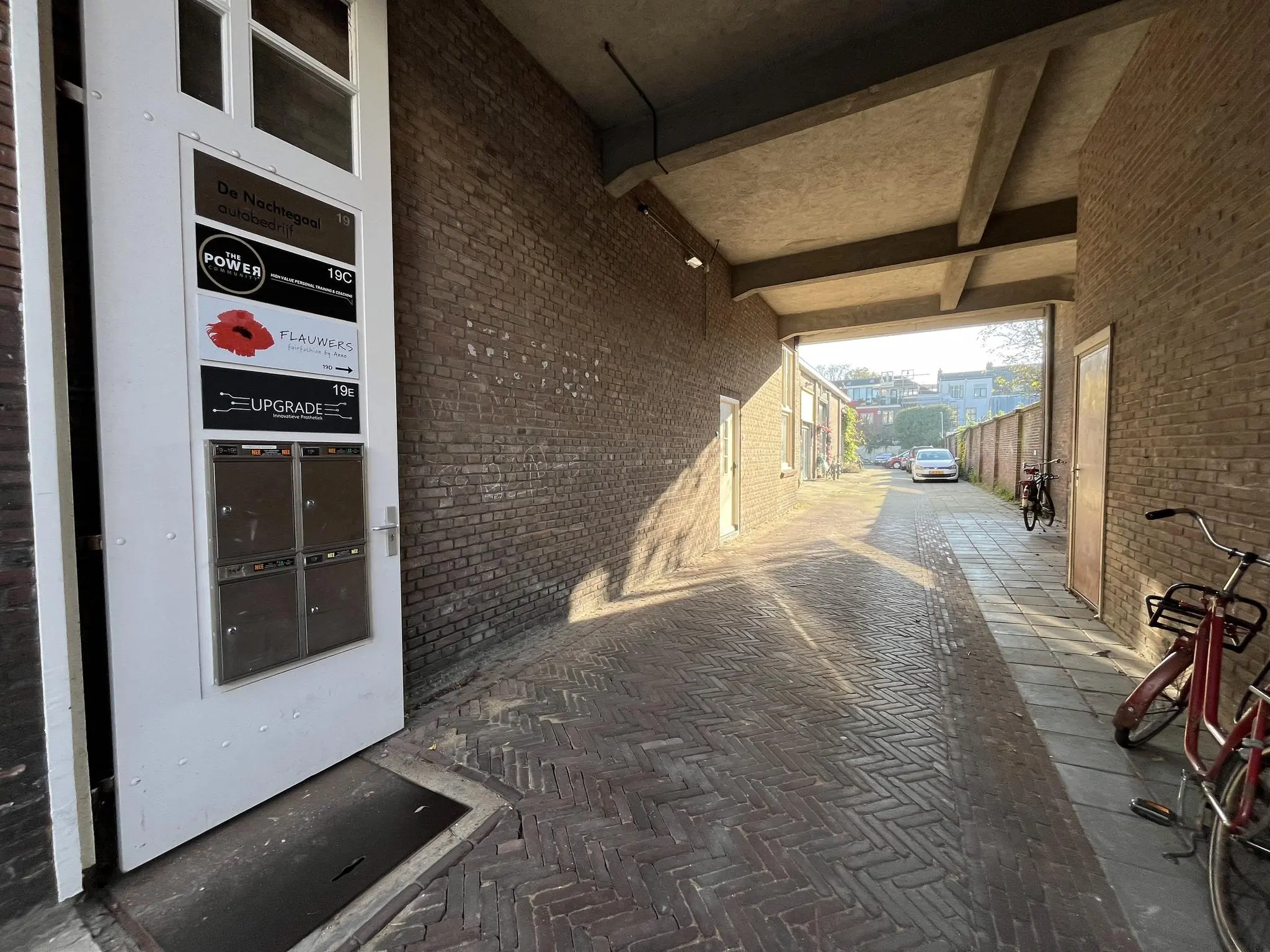 Ingang van meerdere bedrijven aan de Kerkstraat, met zicht op een smalle doorgang en geparkeerde fietsen en auto.