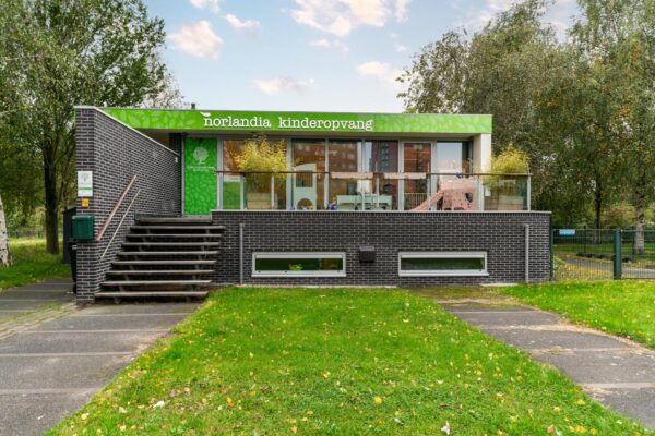 Vooraanzicht van kinderdagverblijf Norlandia Kinderopvang aan de Dedemsvaartweg, met een trap naar de entree en speeltoestellen op het terras.