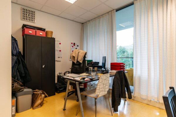 Kantoorruimte aan de Dedemsvaartweg met bureau, stoelen, archiefkasten en een groot raam met lichte gordijnen.