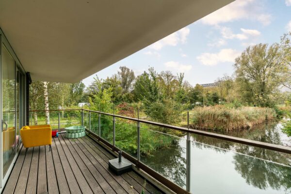 Ruim balkon met houten vlondervloer aan de Dedemsvaartweg, met uitzicht op water en groen.
