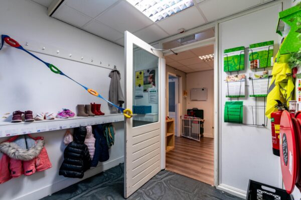 Kinderopvanghal met jasjes, schoenen en informatieborden bij de ingang aan de Dedemsvaartweg.