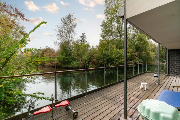 Houten vlonderterras aan het water bij een woning aan de Dedemsvaartweg, omringd door groen en voorzien van kinderspeelgoed.