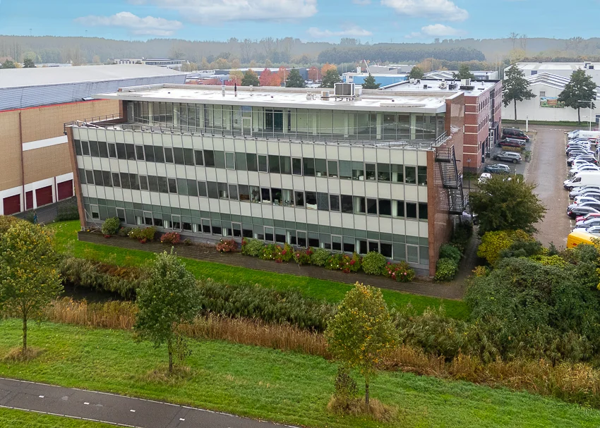 Kantoorgebouw aan de Curieweg met grote ramen en omliggend groen, gezien vanaf de straatzijde.