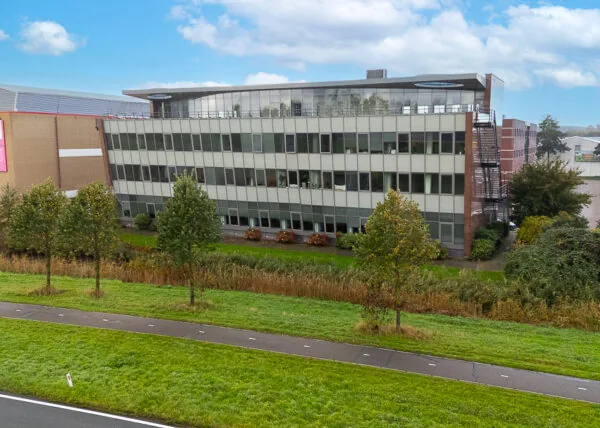 Kantoorgebouw aan de Curieweg met meerdere verdiepingen, gelegen langs een groenstrook met bomen.