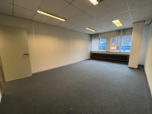Leeg kantoorruimte met grijze vloerbedekking en zicht op Coolblue-gebouw aan de Hollantlaan.