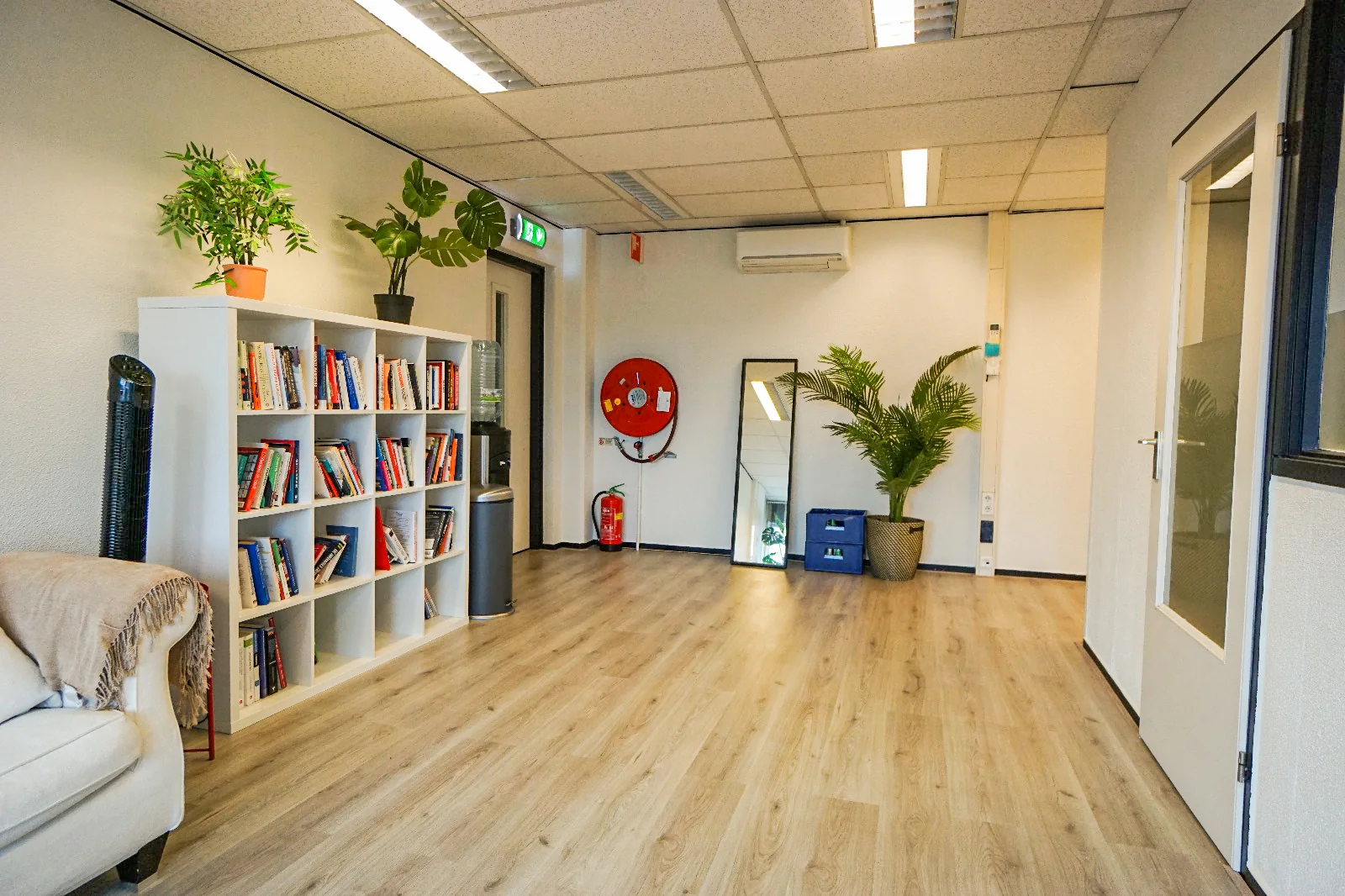 Moderne wachtruimte aan de Hollantlaan met boekenkast, planten, spiegel en waterdispenser.